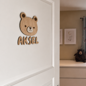 Et navneskilt på barnerommet med personlig, håndlaget navneskilt med bamse og navnet Aksel på hvit dør.