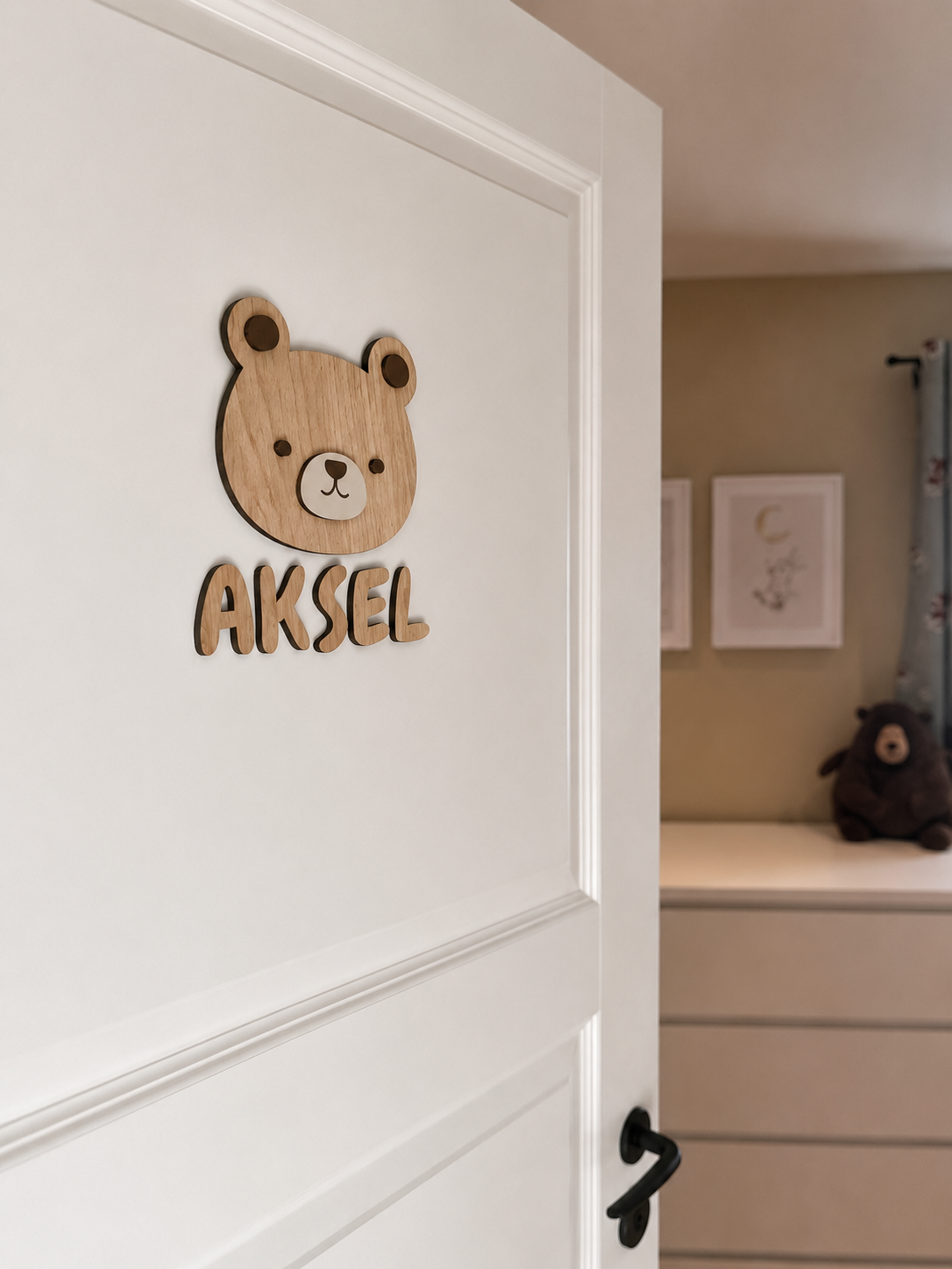 Et navneskilt på barnerommet med personlig, håndlaget navneskilt med bamse og navnet Aksel på hvit dør.
