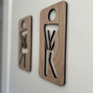 To håndlagde treskilt som humoristiske toalettskilt med figurer – en kvinne og en mann i tre med utskjærte kropper.