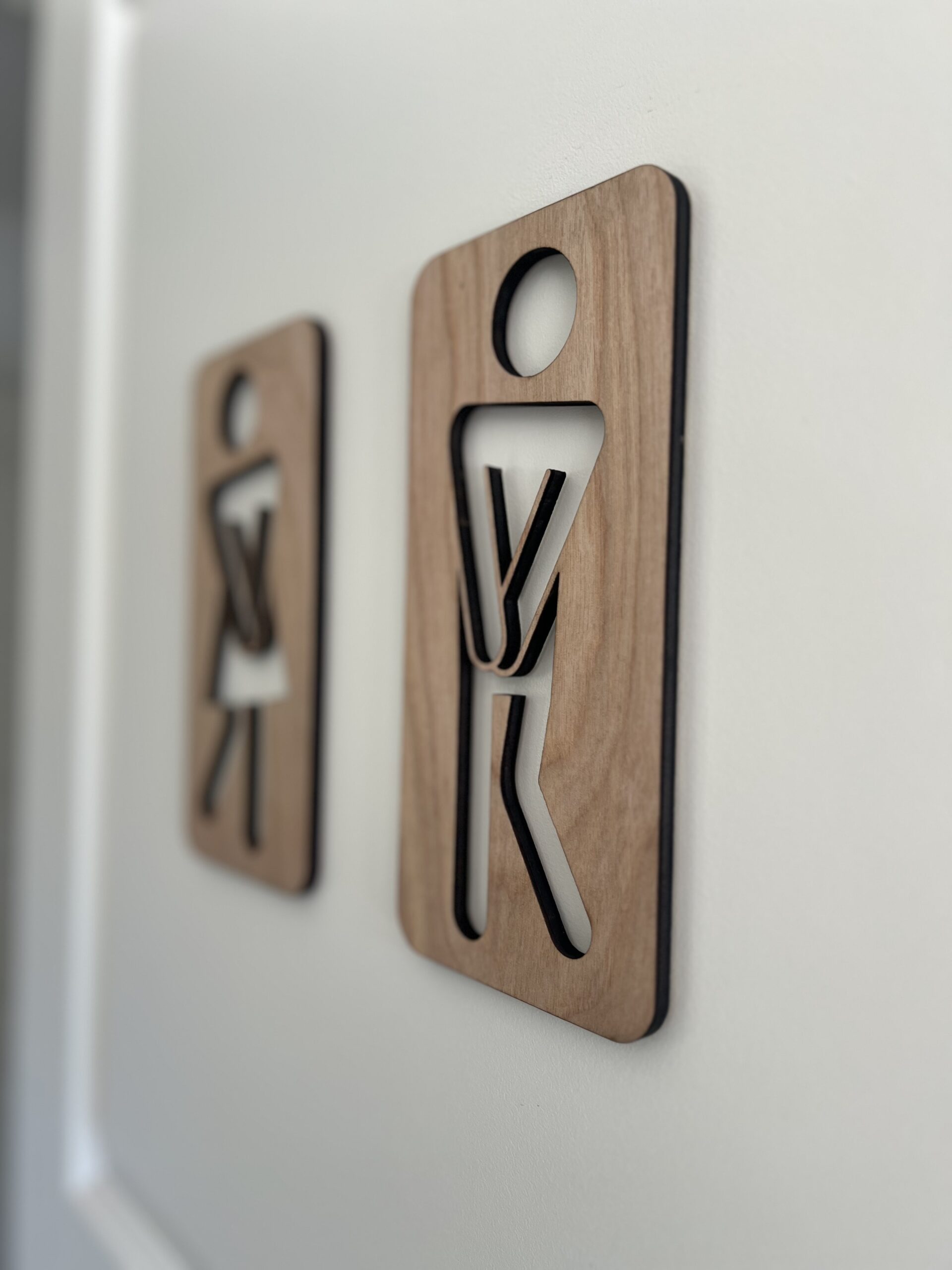 To håndlagde treskilt som humoristiske toalettskilt med figurer – en kvinne og en mann i tre med utskjærte kropper.