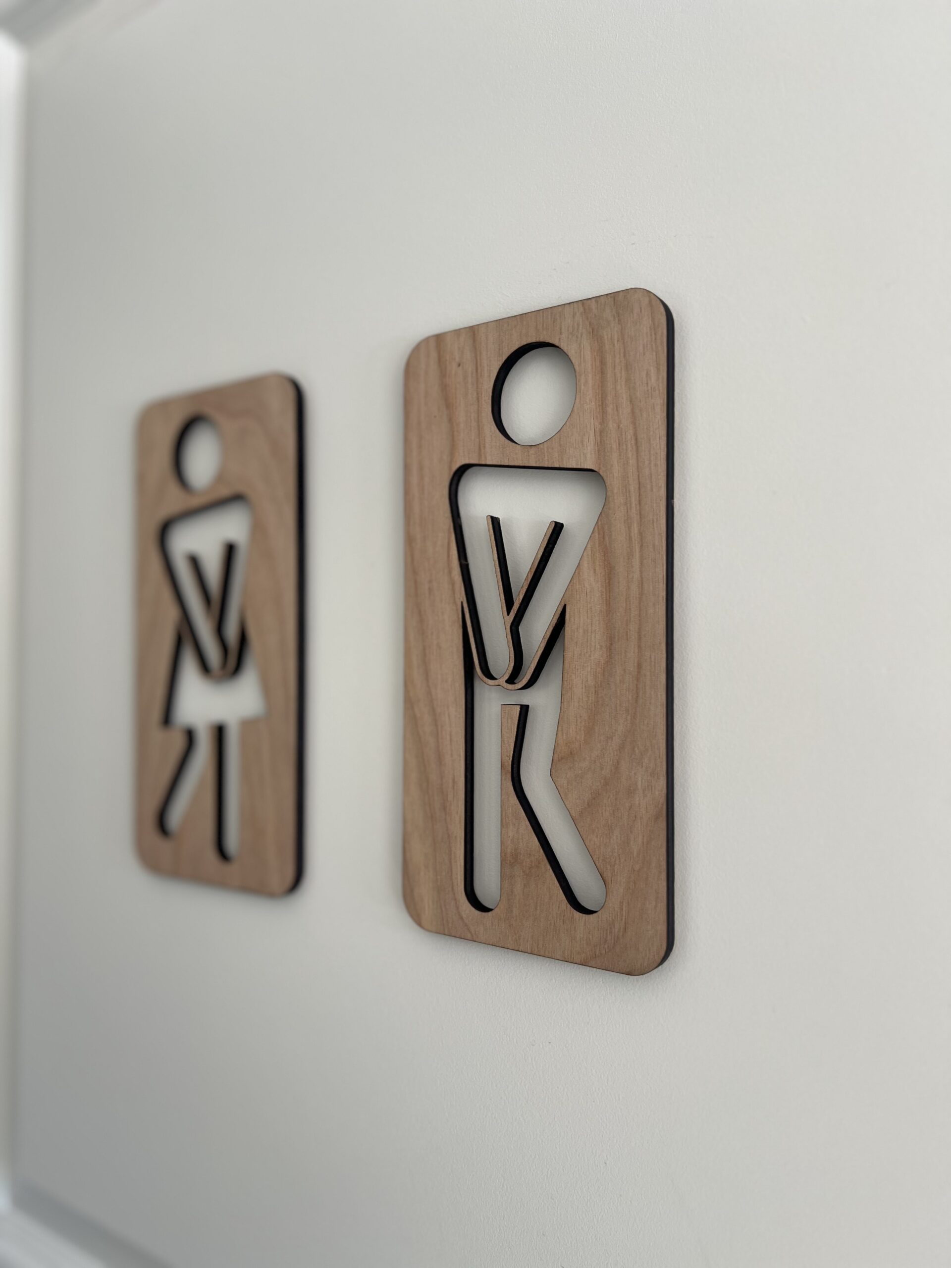 To håndlagde treskilt som humoristiske toalettskilt med figurer – en kvinne og en mann i tre med utskjærte kropper.