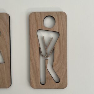 To håndlagde treskilt som humoristiske toalettskilt med figurer – en kvinne og en mann i tre med utskjærte kropper.