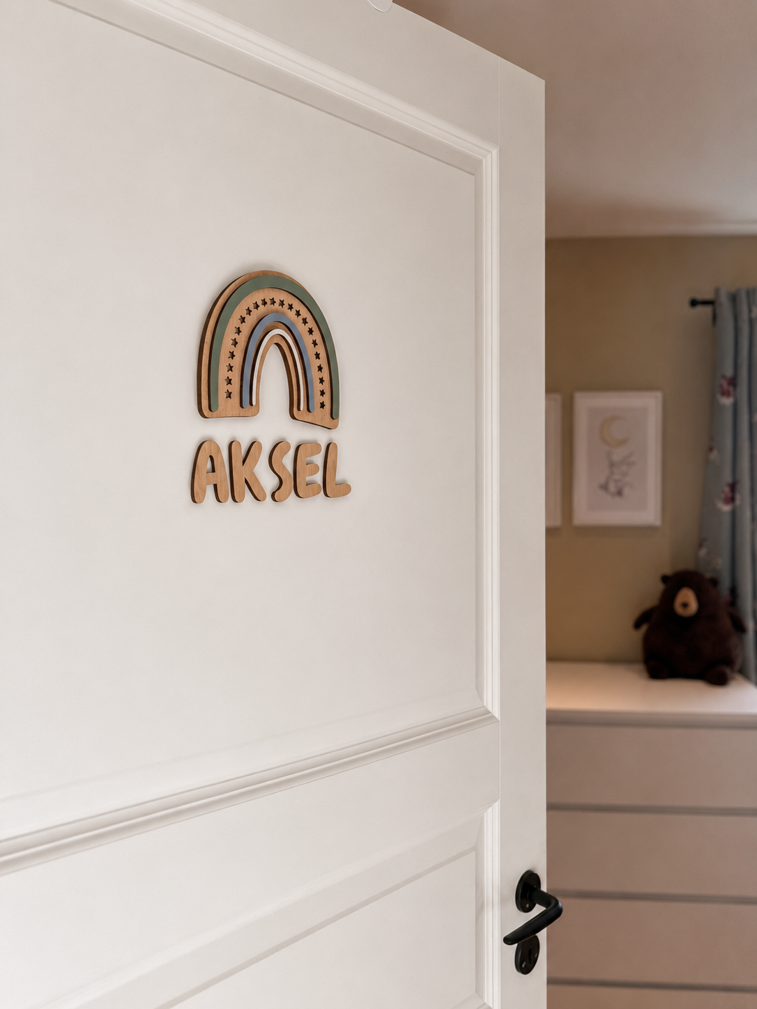 Navneskilt til barnerom med en håndlaget blå regnbue som henger over barnets navn.