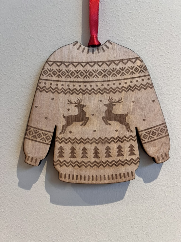 Julekule i tre formet som strikkegenser med gravert julemotiv og rødt bånd.