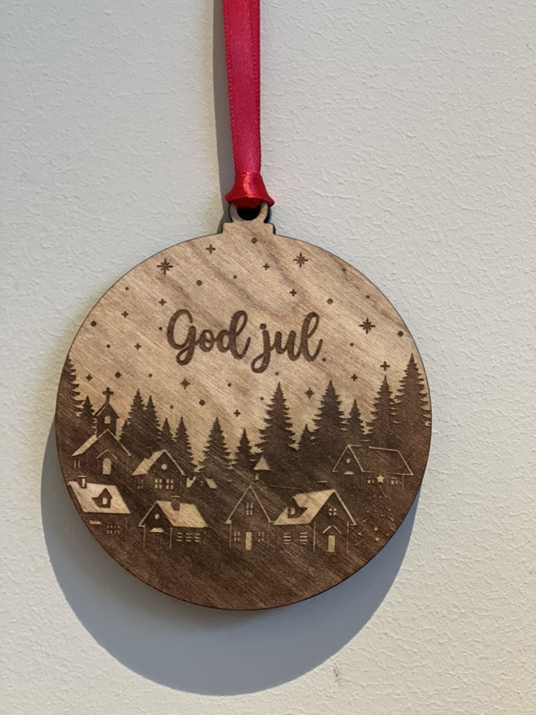 En lasergravert julekule av en landsby dekket av snø.