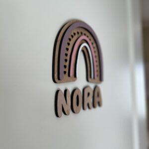 Navneskilt til barnerom med en håndlaget rosa regnbue som henger over barnets navn.