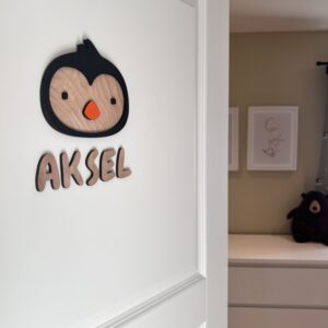 Navneskilt til barnerom med en håndlaget pingvin som henger over barnets navn.
