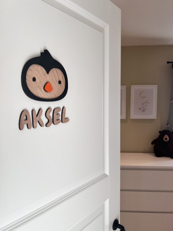 Navneskilt til barnerom med en håndlaget pingvin som henger over barnets navn.