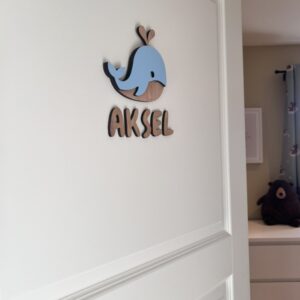 Navneskilt til barnerom med en håndlaget hval som henger over barnets navn.