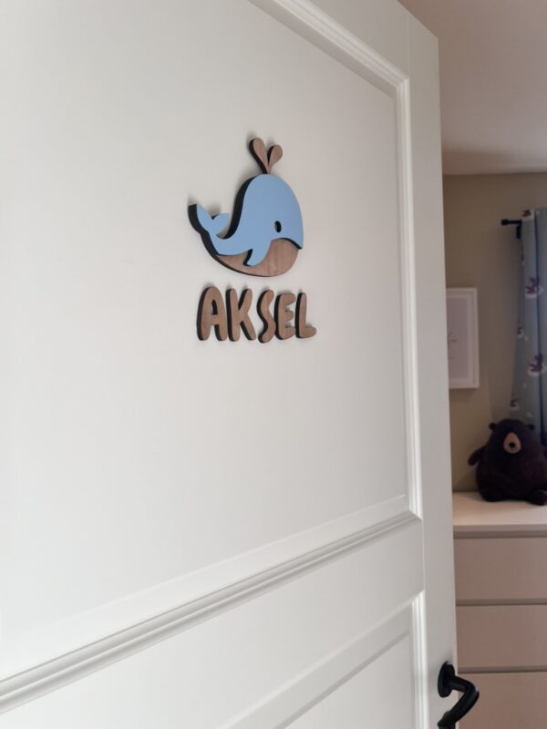 Navneskilt til barnerom med en håndlaget hval som henger over barnets navn.