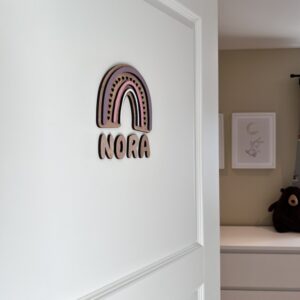 Navneskilt til barnerom med en håndlaget rosa regnbue som henger over barnets navn.