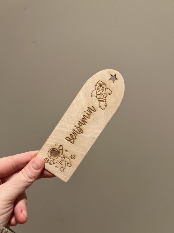 Personlig lasergravert bokmerke i 3 mm bjørkefiner med astronaut, rakett, stjerner og barnets navn, perfekt for barn som liker å lese.