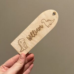 Personlig lasergravert bokmerke i 3 mm bjørkefiner med dinosaurmotiv og barnets navn, perfekt for barn som liker å lese.