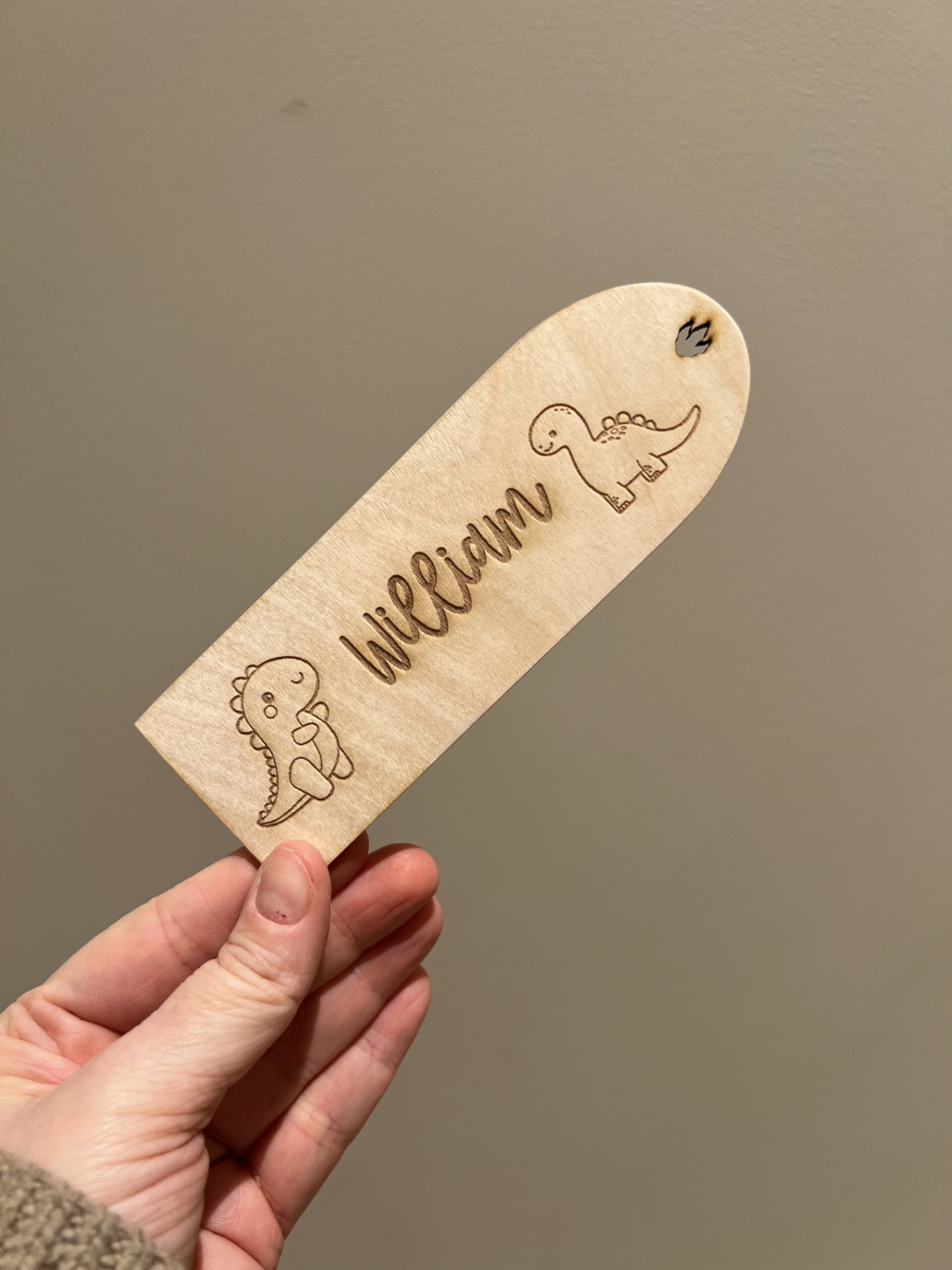 Personlig lasergravert bokmerke i 3 mm bjørkefiner med dinosaurmotiv og barnets navn, perfekt for barn som liker å lese.