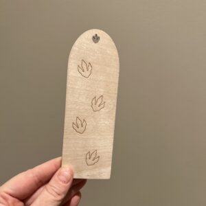Baksiden av et personaliserbart bokmerke med dinosaurer, bak er det lasergraverte dinosaurfotspor.
