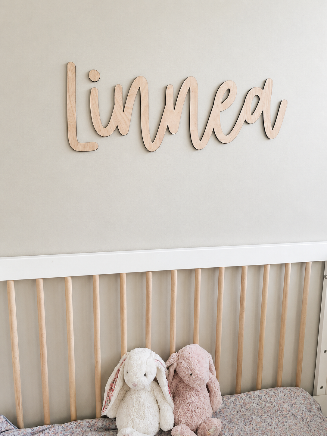 Treskiltet med navnet «Linnea» hengt på veggen over en barneseng med to kosebamser i form av kaniner.