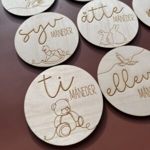 Detaljbilde av milepælskort i tre med lasergravert illustrasjon og norsk tekst.