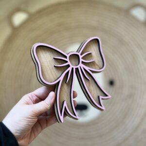Håndlaget sløyfeformet veggdekor fra ByRossland i bjørkfiner med rosa detaljer, perfekt som personlig pynt på barnerommet.