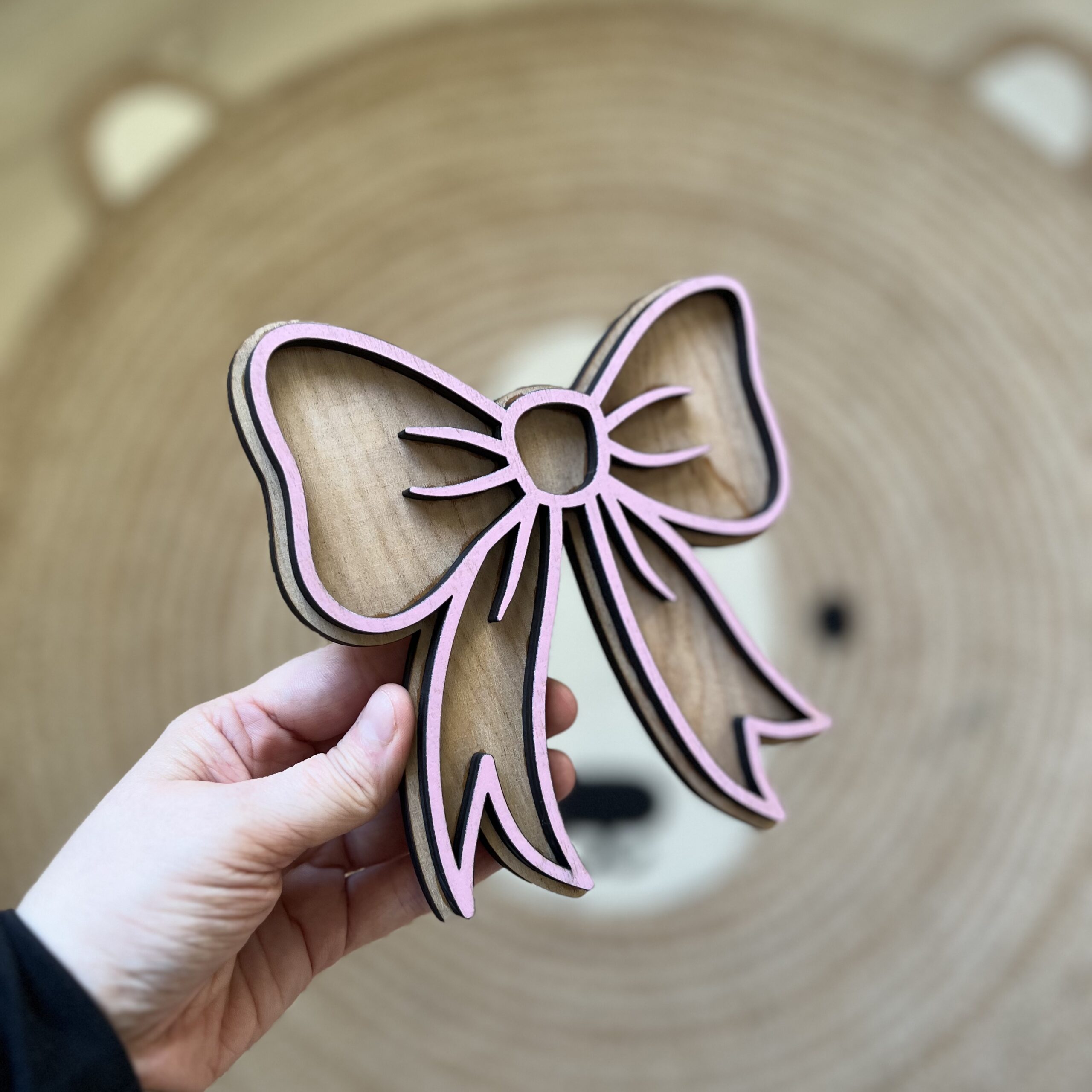 Håndlaget sløyfeformet veggdekor fra ByRossland i bjørkfiner med rosa detaljer, perfekt som personlig pynt på barnerommet.