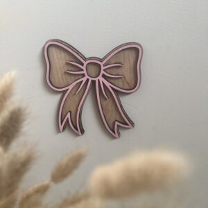 Sløyfe veggfigur i bjørkfiner med rosa overlag fra ByRossland, tidløs og dekorativ detalj til baby- og barnerom.
