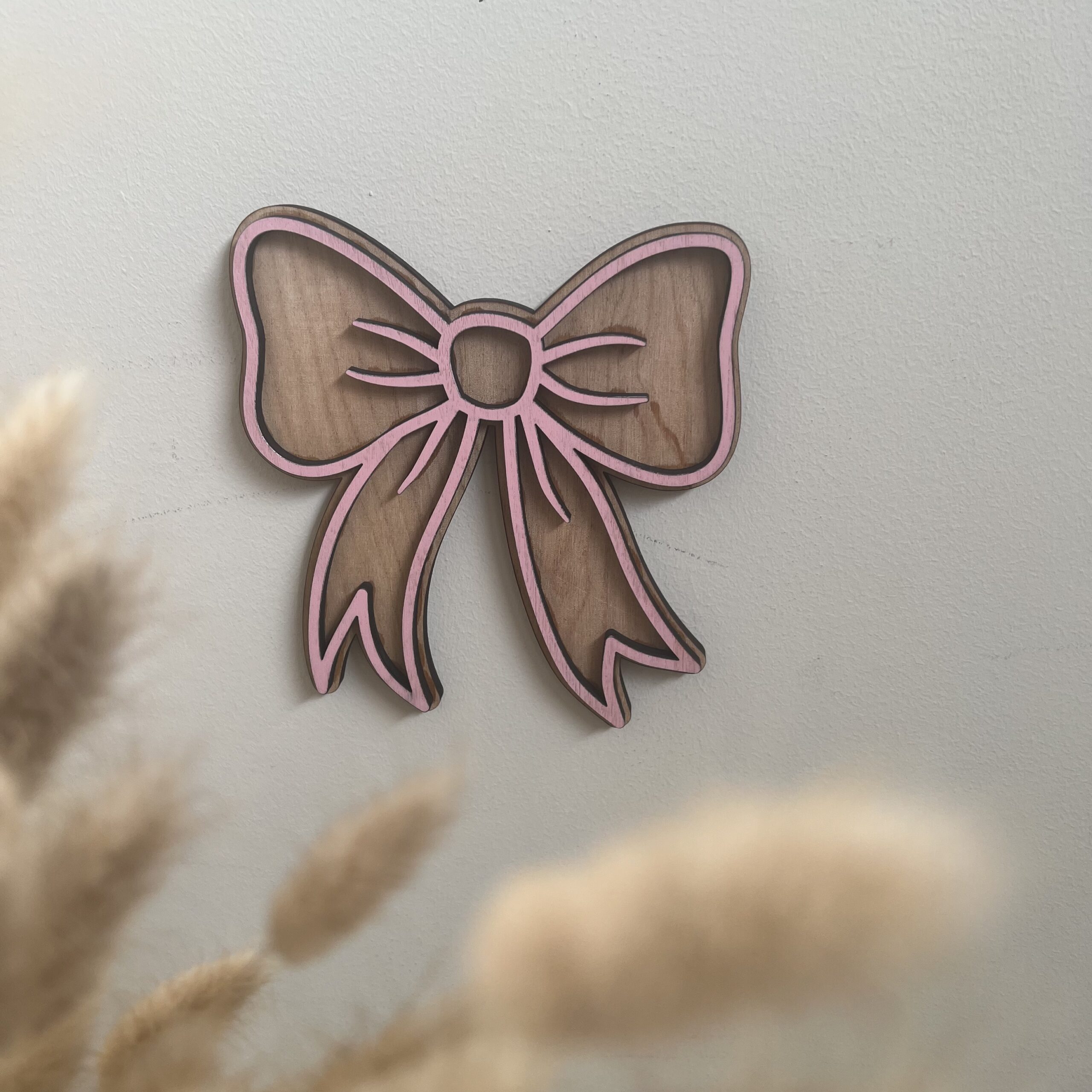 Sløyfe veggfigur i bjørkfiner med rosa overlag fra ByRossland, tidløs og dekorativ detalj til baby- og barnerom.