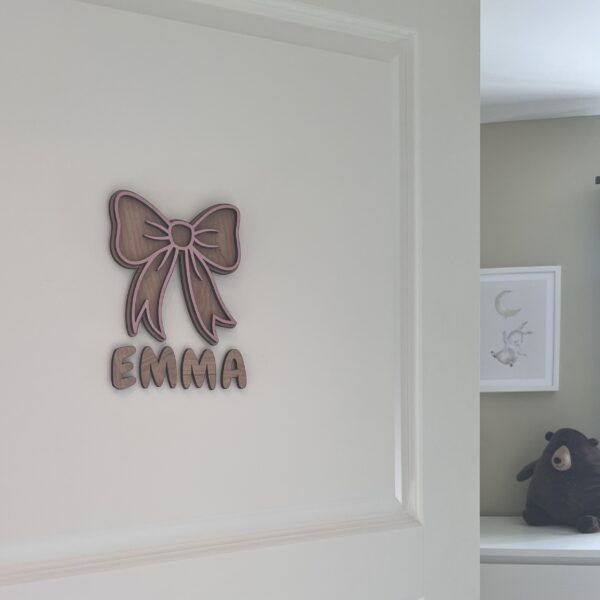 Håndlaget navneskilt med barnets navn og en rosa sløyfe i bjørkfiner fra ByRossland, perfekt til barnerom eller babyrom.
