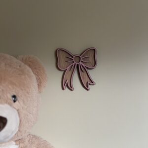 Håndlaget sløyfeformet veggdekor fra ByRossland i bjørkfiner med rosa detaljer, perfekt som personlig pynt på barnerommet.