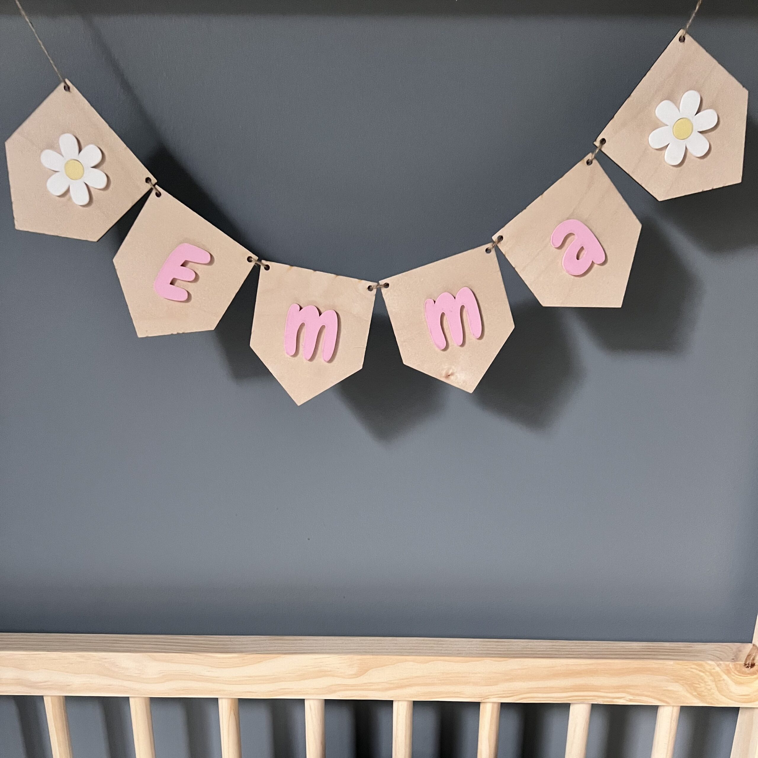 Personlig girlander med navn i rosa akryl til barnerommet med to endreflagg med hvite blomster.