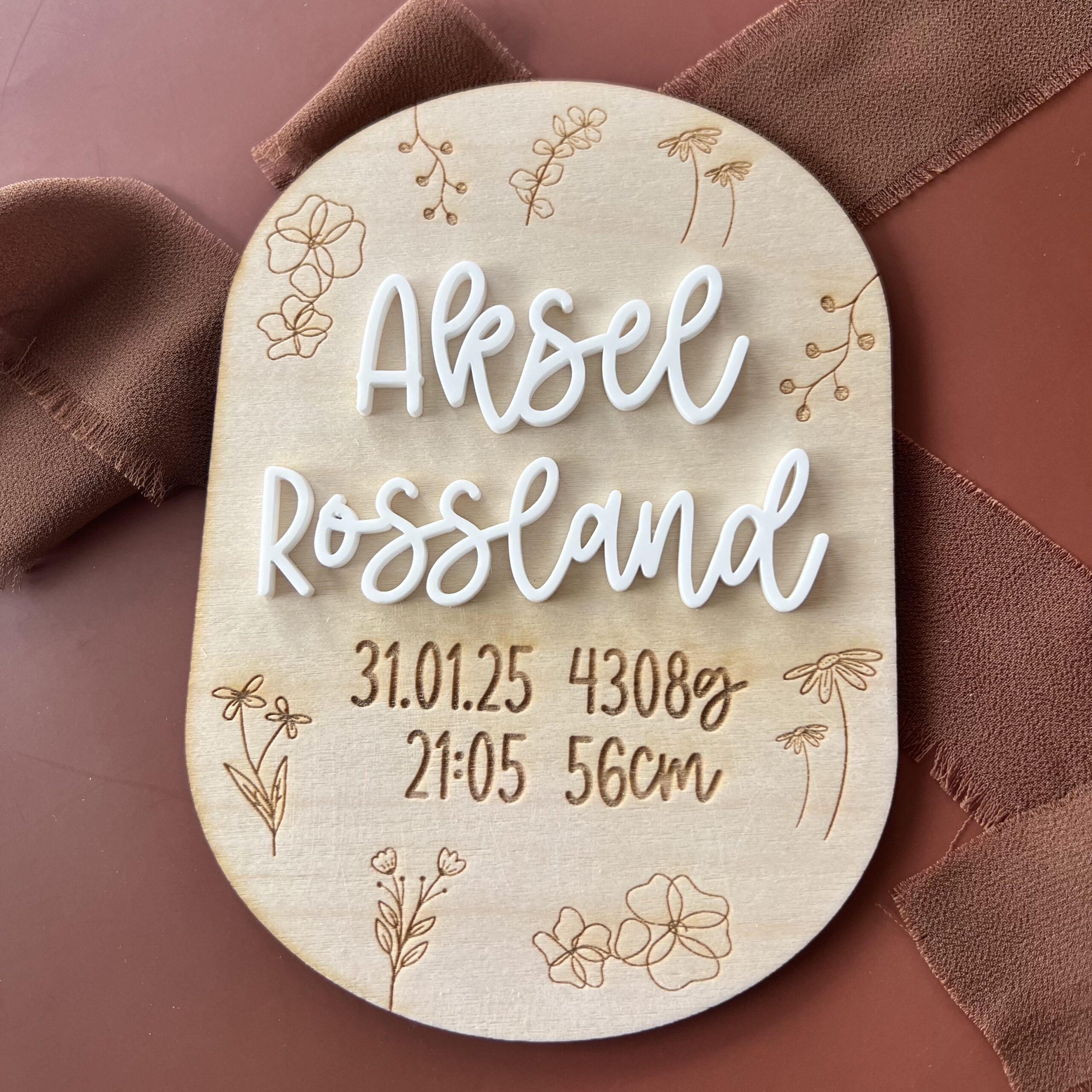 Personlig fødselsskilt med graverte blomster i bjørkfiner med barnets navn i hvit akryl og graverte fødselsdetaljer — håndlaget av ByRossland