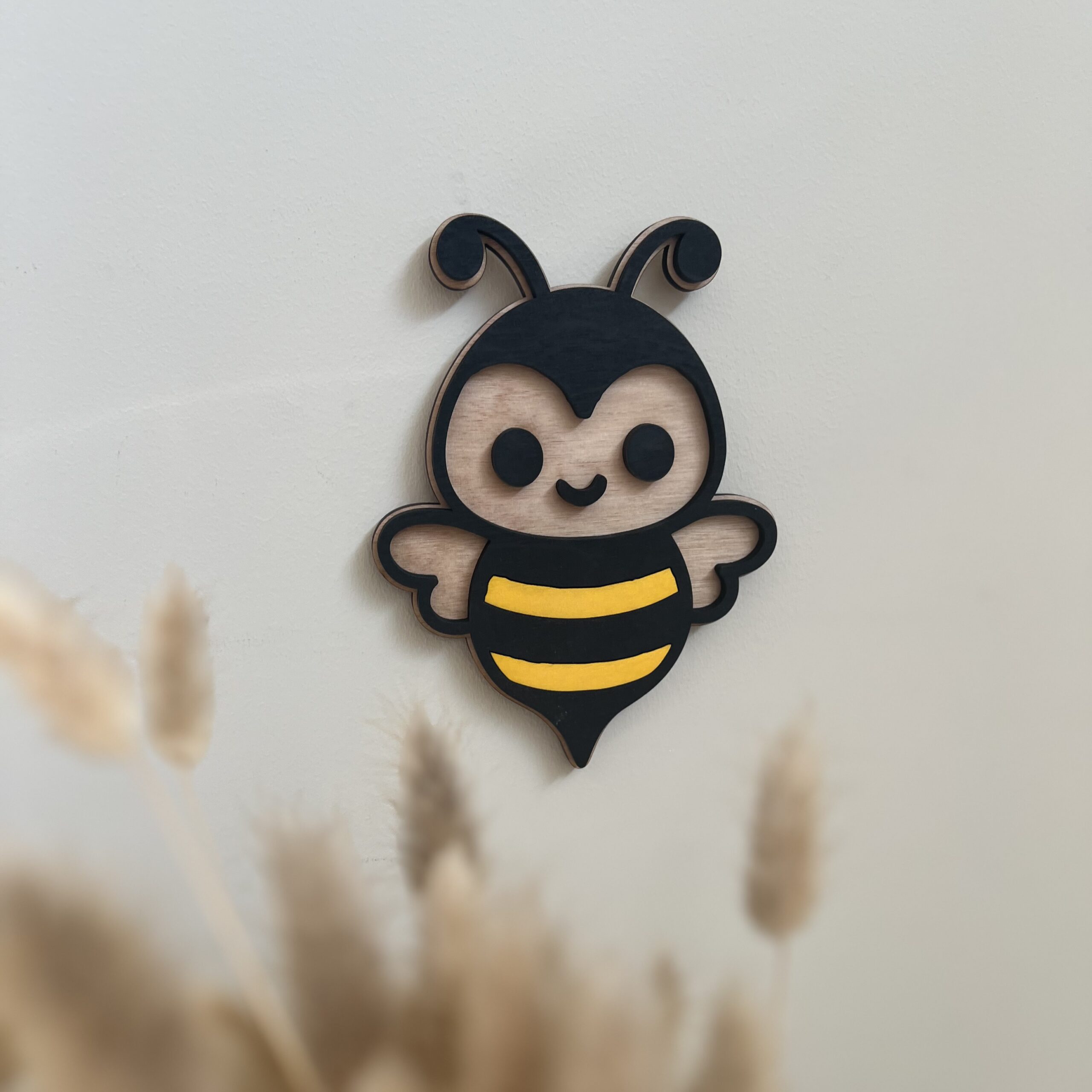 En håndlaget bie veggfigur henger på en beige vegg. Perfekt til barnerommet som et søtt blikkfang eller sammen med navn som navneskilt.