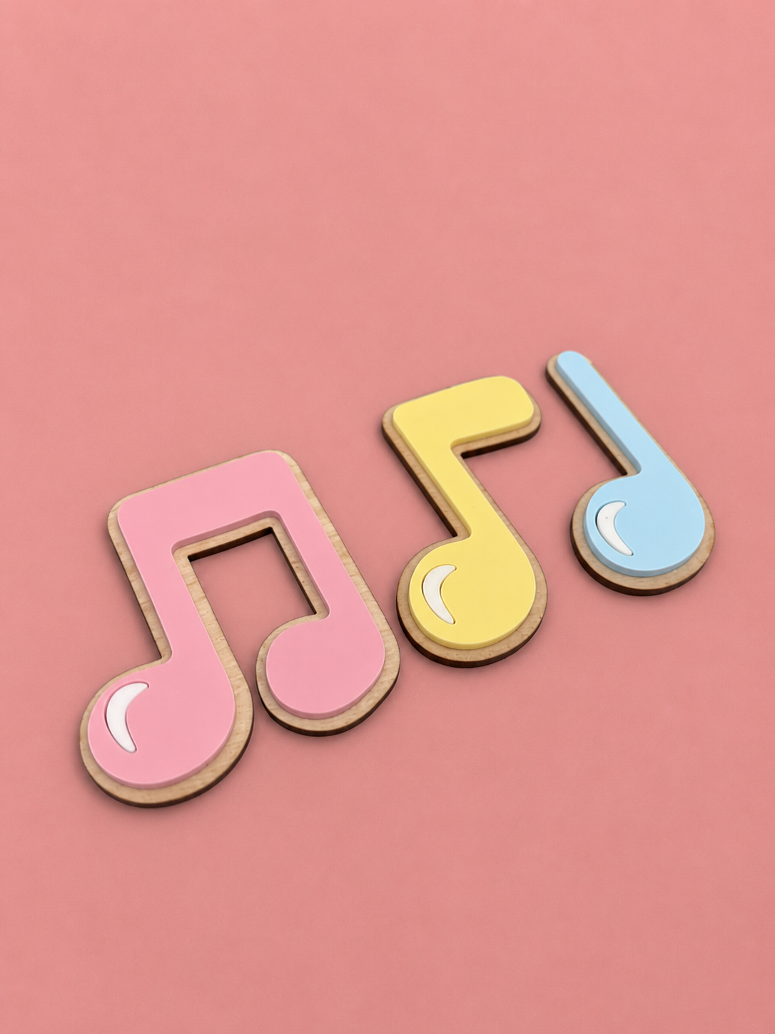 Tre fargerike tredekorasjoner formet som musikknoten i rosa, gul og blå mot rosa bakgrunn.