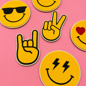 Gule emoji-klistremerker med solbriller, stjerne-øyne, hjerte, lyn-øyne og håndtegn på rosa bakgrunn